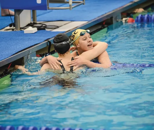 Two swimmers in a pool hug after a race